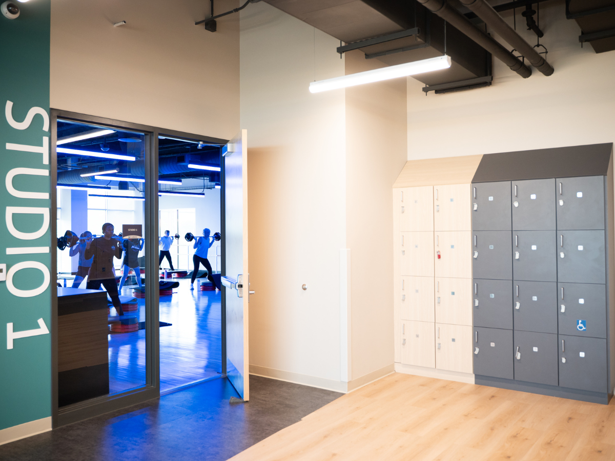 People lifting weights in a gym seen through an open door, with a teal wall reading 'STUDIOS' on the left.